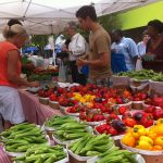 Vendor selling okra, red and yellow bell peppers to shoppers under a tent