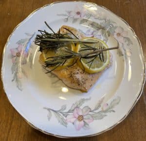 Baked Salmon topped with lemon slices and rosemary on china plate