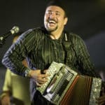 Louisiana Zydeco artist Terrance Simien plays the accordion against a black background.