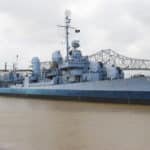 Gray battleship in river with bridge in rear