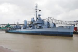 Gray battleship in river with bridge in rear