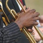 African-American person in blue pin-striped suit holds gold trumpet