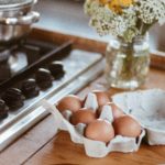 Eggs in carton next to stove with pot and flowers in vase