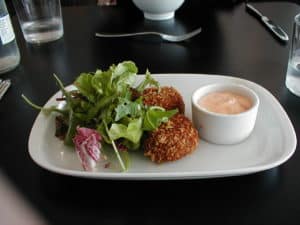 Crab cakes served on white plate with greens and sauce