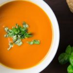 Creamy tomato basil soup with sprig of basil on the side