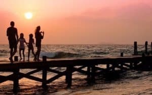 Family on pier at sunset with orange sky.