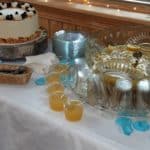 White cake on white tablecloth and punch bowl with blue flower petals