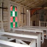 Inside of old church showing red and green stained glass windows and white pews