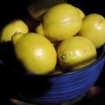 Yellow lemons in blue bowl on black backgound