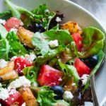 White bowl of salad greens, romano cheese bits, olives, cherry tomatoes