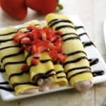 4 crepes on white plate with strawberries and chocolate topping