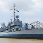 USS KIDD ship docked at the wharf on the muddy Mississippi River with bridge in background.
