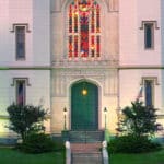 Old courthouse with white walls, stained-glass windows, blue sky, green grass with stairs leading to green front door