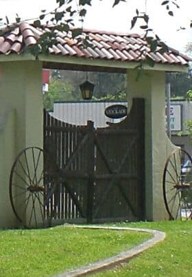 Gate with stucco white walls, brown gate, wagon wheels in front