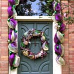 Front door trimmed with purple and gold swag with green balls and matching wreath on door.